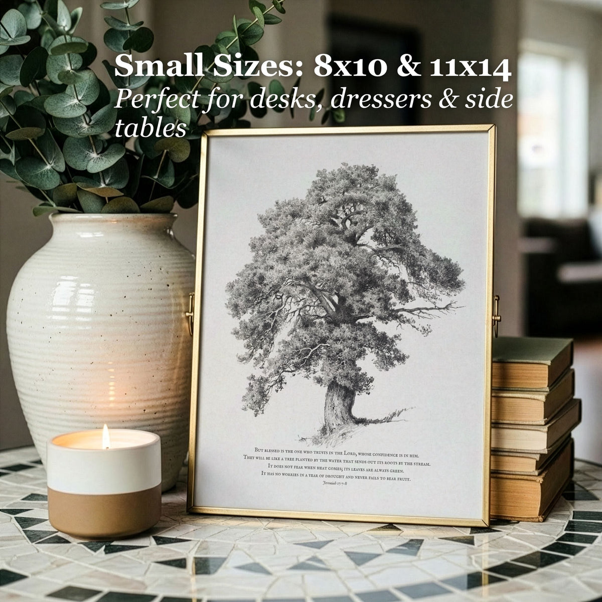 A framed black-and-white tree illustration print displayed on a mosaic table, styled with a ceramic vase of eucalyptus, a lit candle, and stacked books. White text at the top reads: 'Small Sizes: 8x10 & 11x14 Perfect for desks, dressers & side tables.