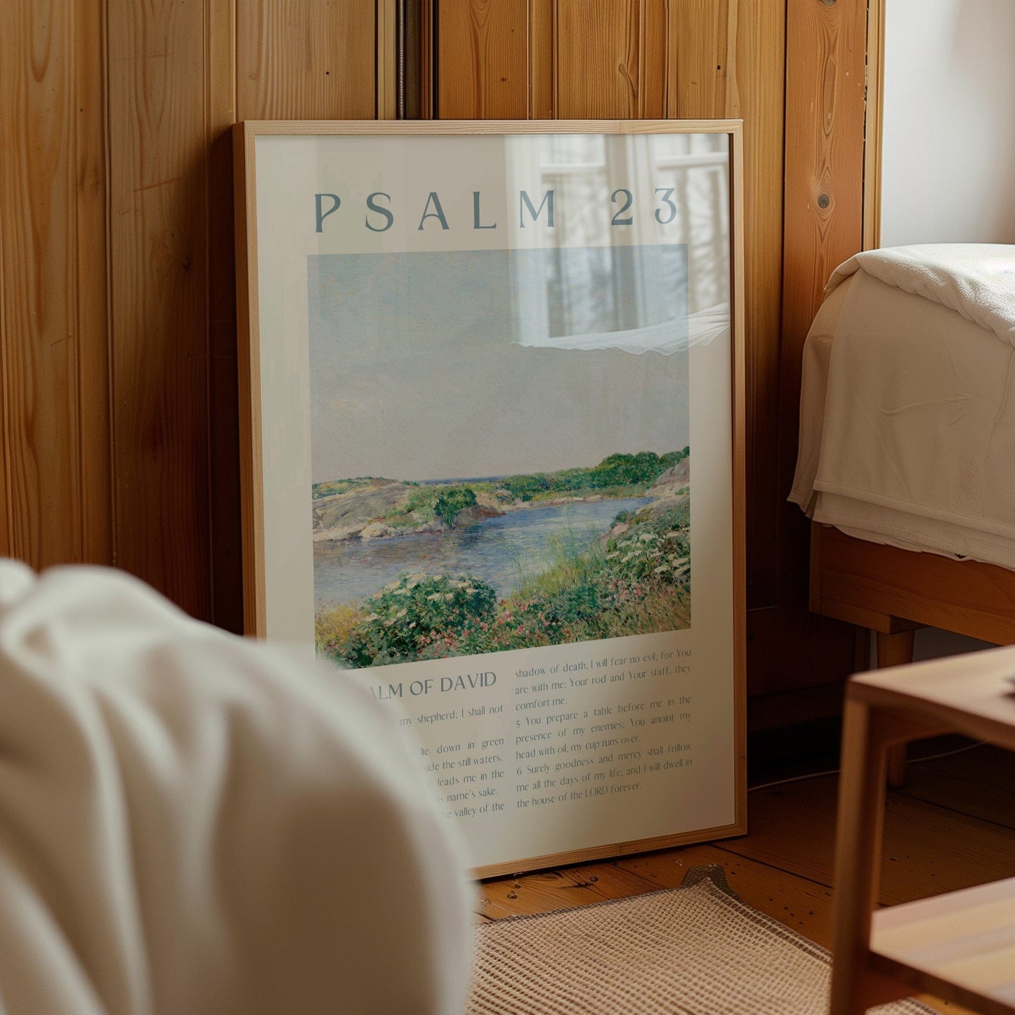 Framed poster with 'Psalm 23' text and landscape illustration in a room with wooden walls and furniture.