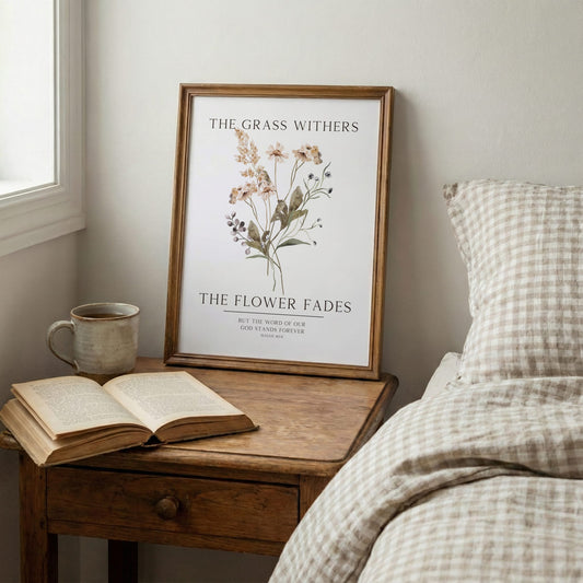 Framed artwork with floral design and text on a wooden nightstand next to an open book and mug.