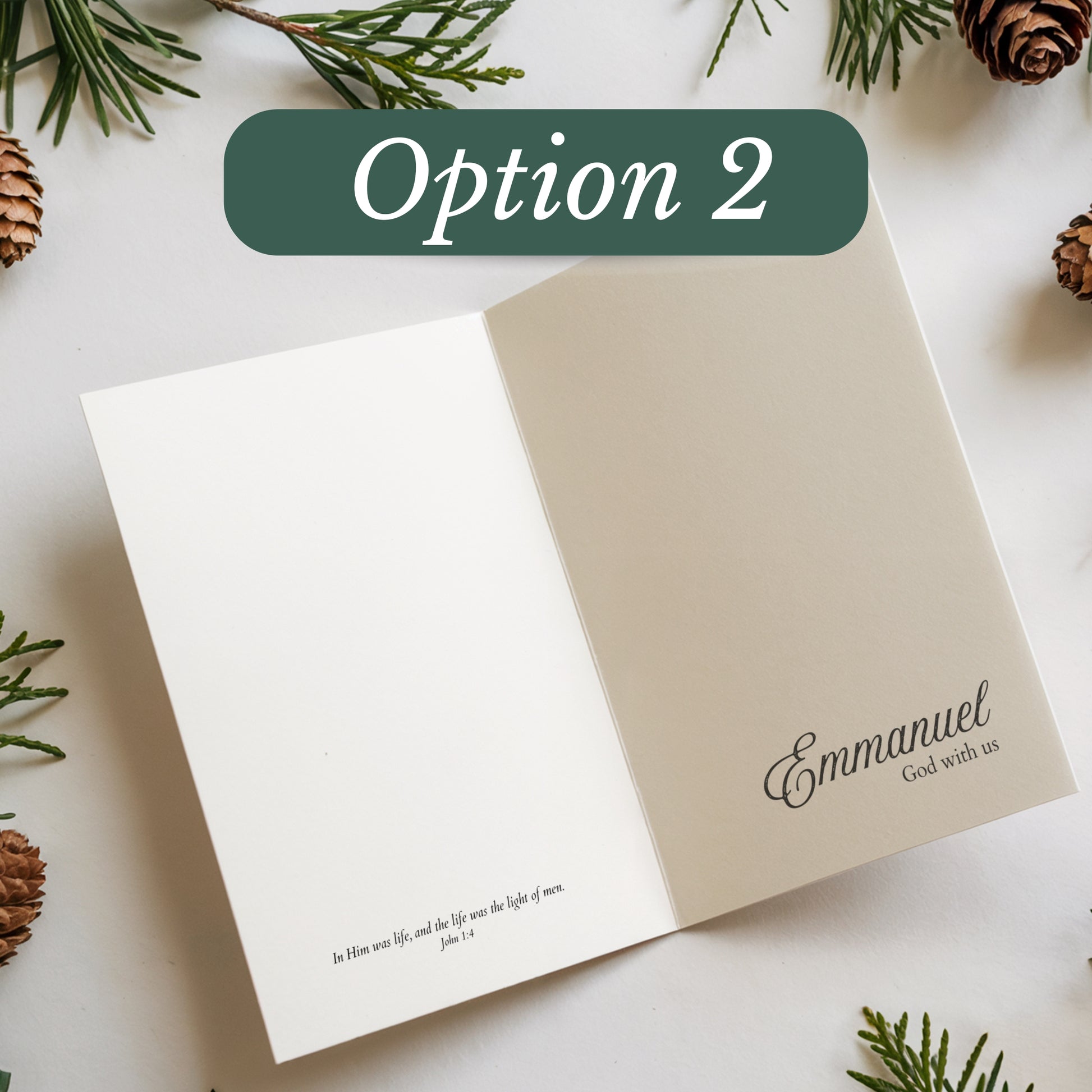Open card with 'Emmanuel' text on a white surface with pine branches and cones.