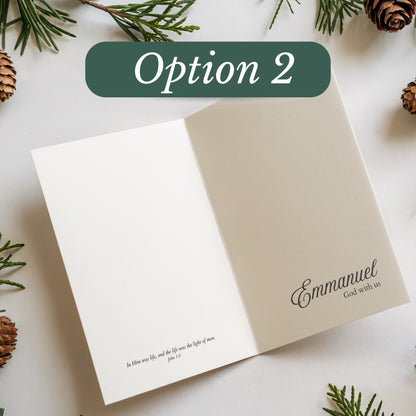 Open card with 'Emmanuel' text on a white surface with pine branches and cones.