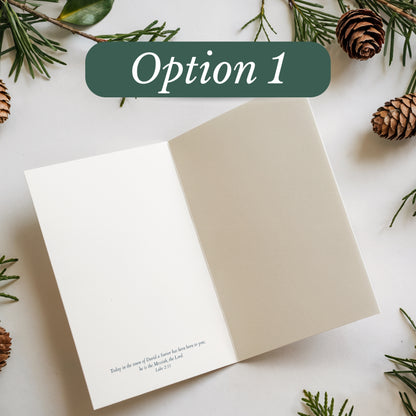 Open card with text on a white surface surrounded by greenery and pine cones