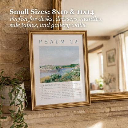 A framed wall art print leaning on a stone ledge in a home interior. The frame is gold-toned and contains a Psalm 23 print with a landscape illustration and text.