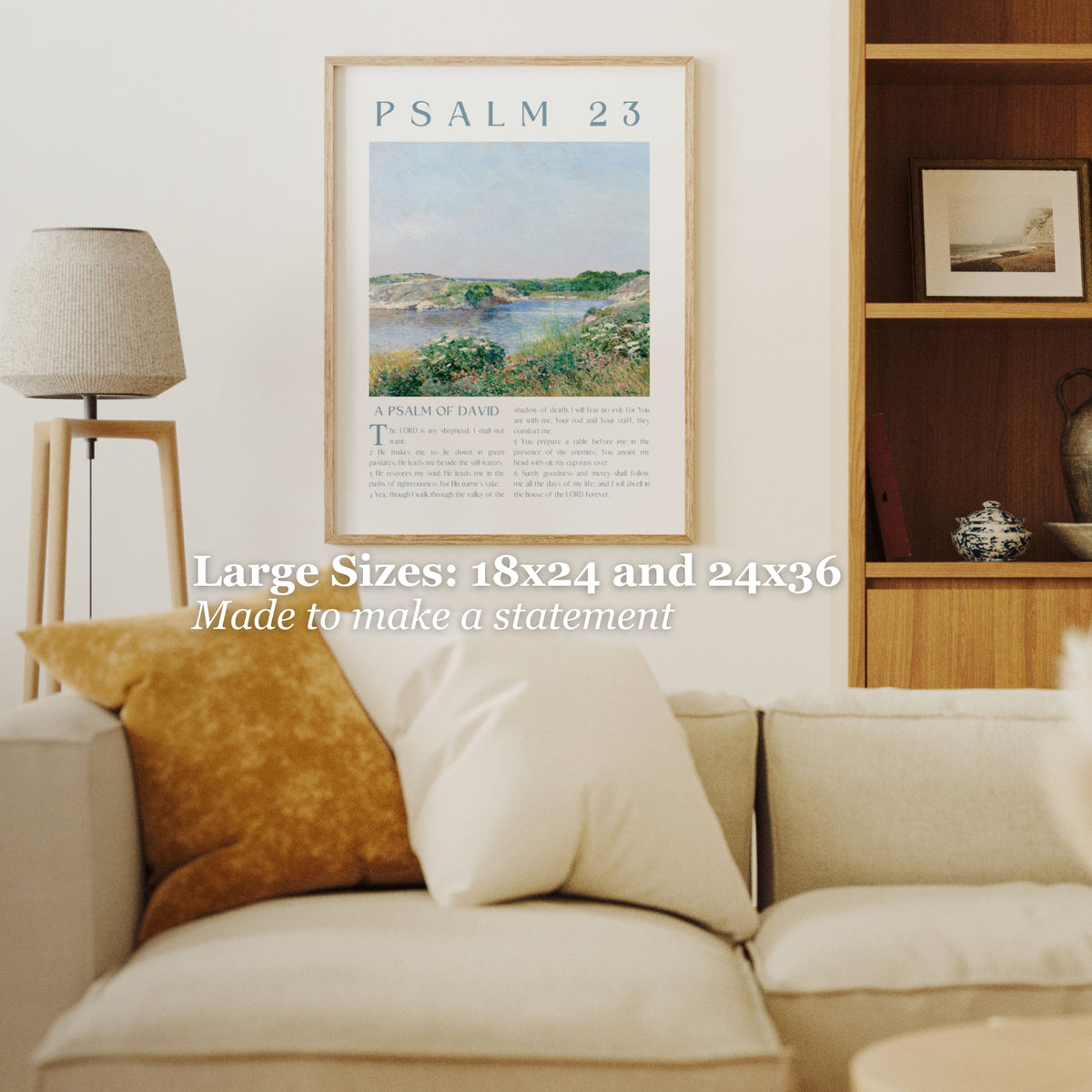 A framed art print of Psalm 23 hanging on a white wall in a modern living room setting. The print features a landscape painting with a river and greenery, framed in a light wood frame.