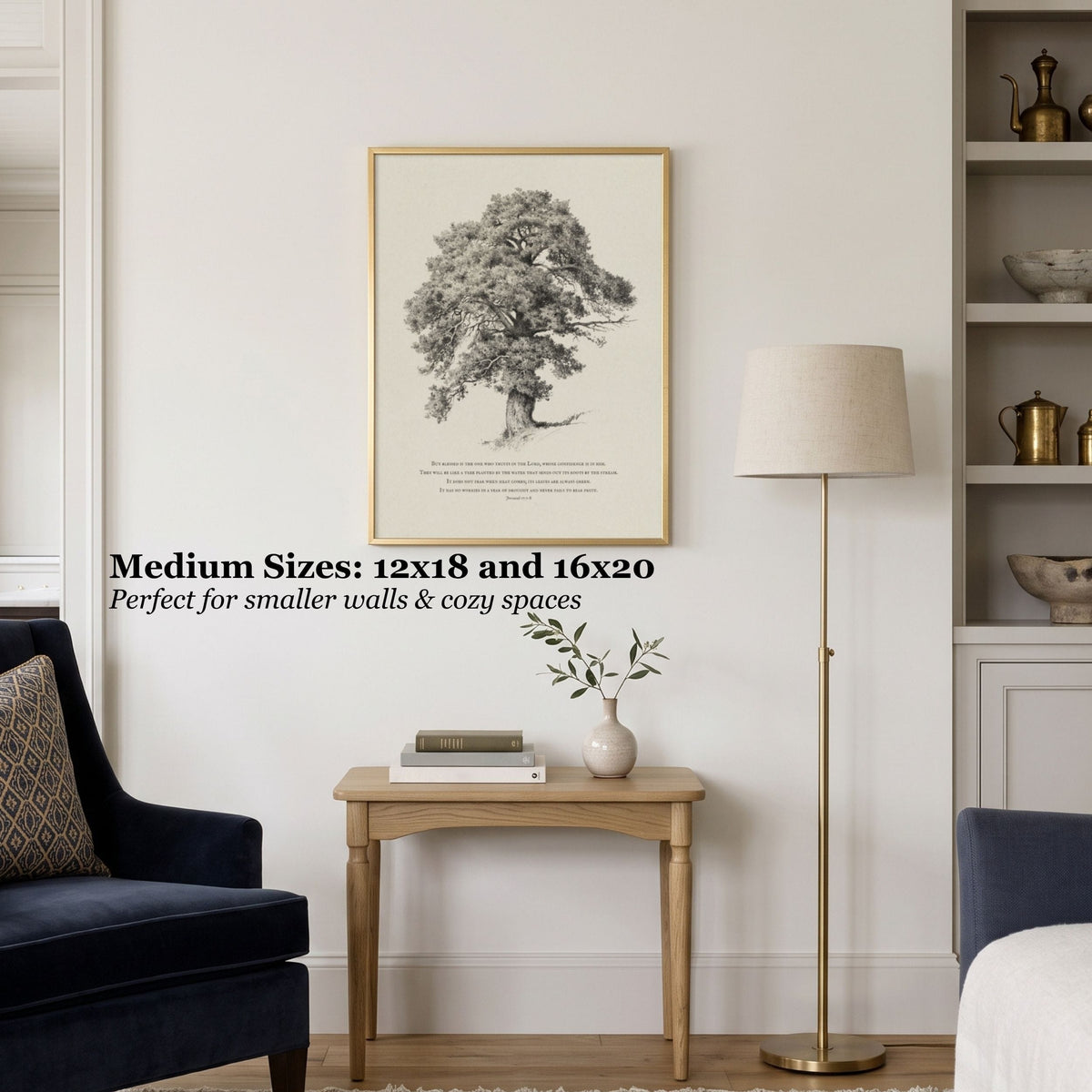 A framed black-and-white tree art print hangs on a light wall above a small wooden side table in a styled room with a navy armchair, floor lamp, and shelving. Text on the image reads: 'Medium Sizes: 12x18 and 16x20 Perfect for smaller walls & cozy spaces.