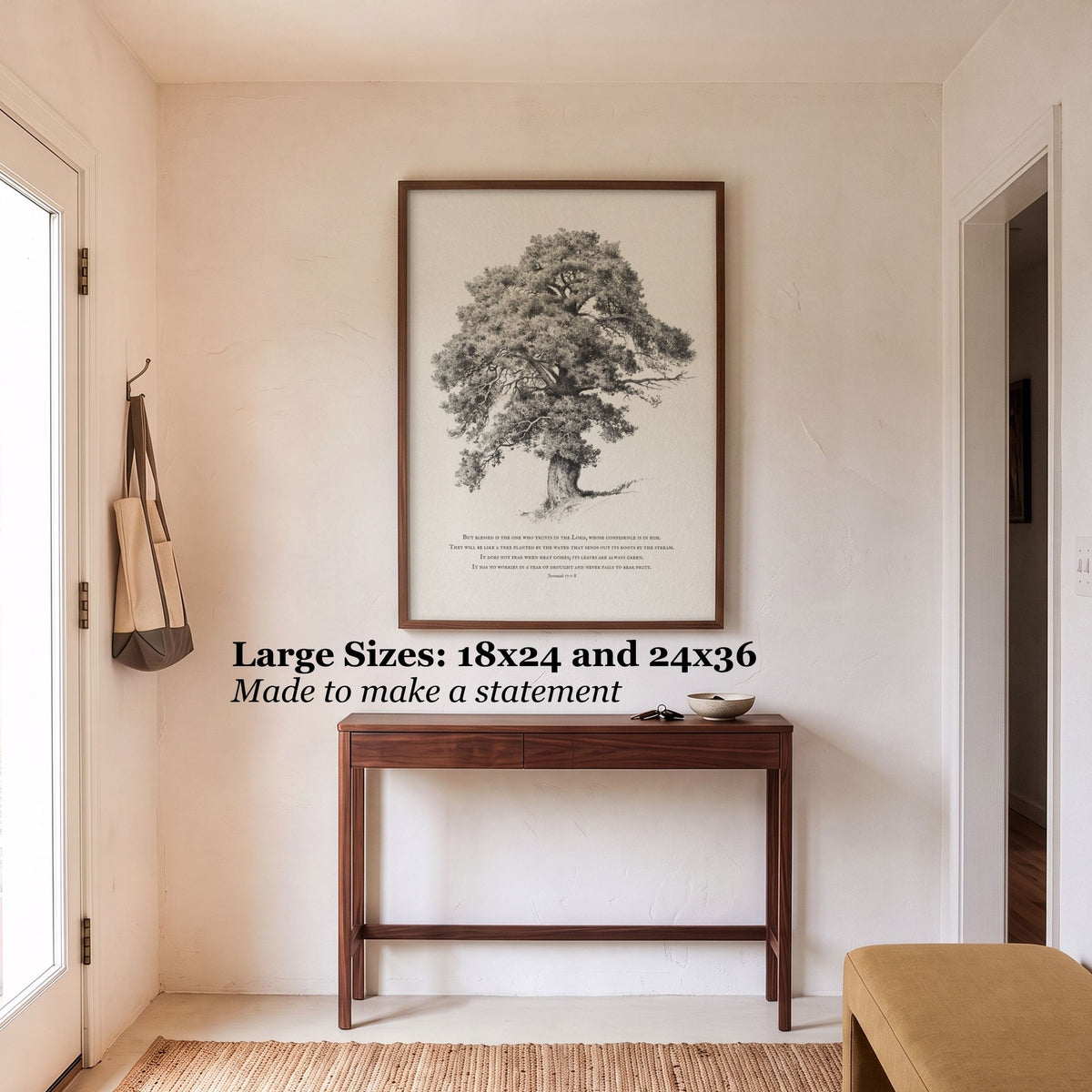 A framed botanical art print of a tree hangs on a beige wall above a dark wood console table in a bright entryway. Text on the image reads: 'Large Sizes: 18x24 and 24x36 Made to make a statement'.