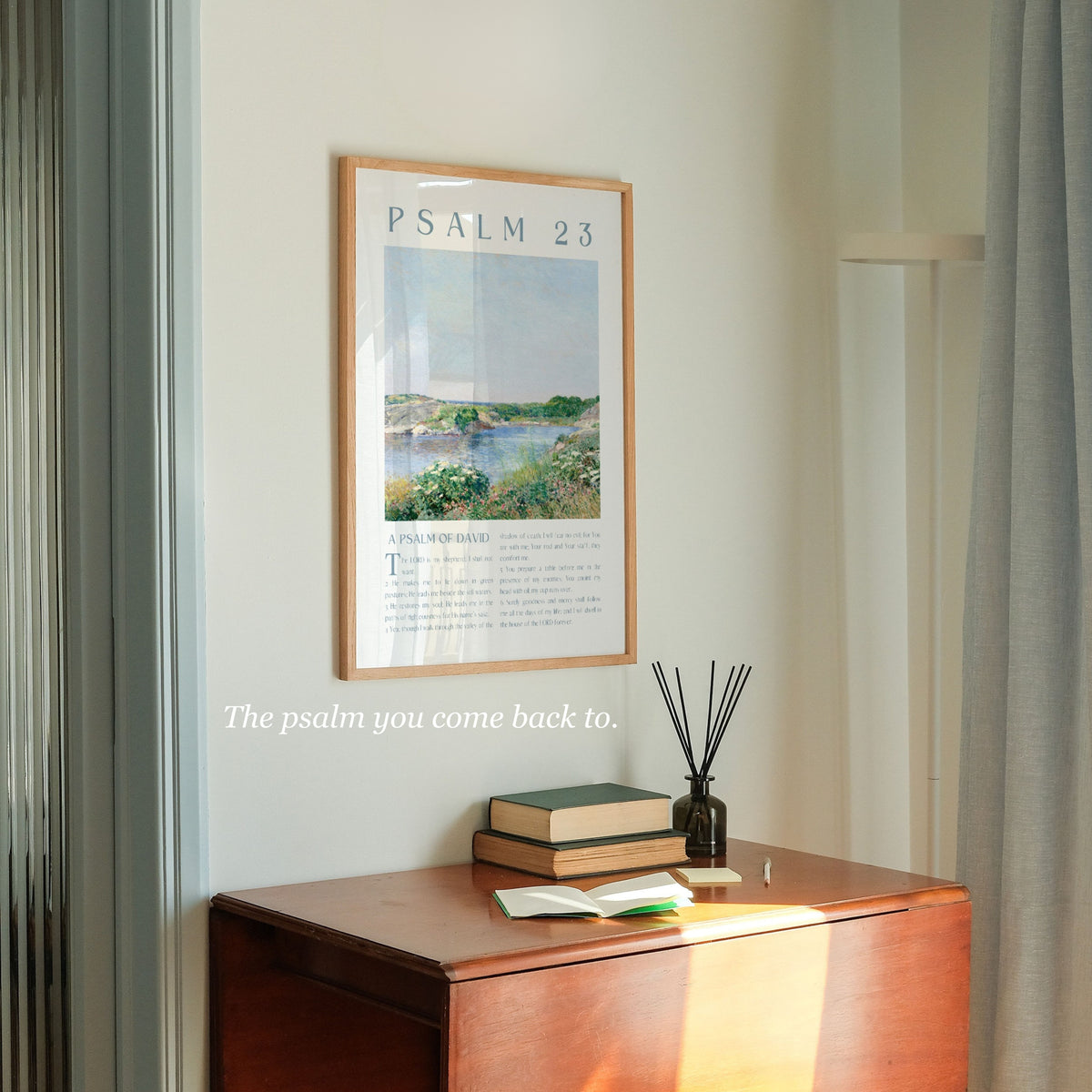 A framed art print of Psalm 23 hanging on a light beige wall above a wooden console table. The print features a landscape painting with the text 'PSALM 23' at the top.