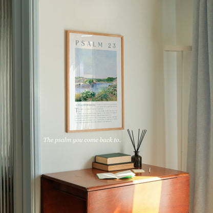 A framed art print of Psalm 23 hanging on a light beige wall above a wooden console table. The print features a landscape painting with the text 'PSALM 23' at the top.