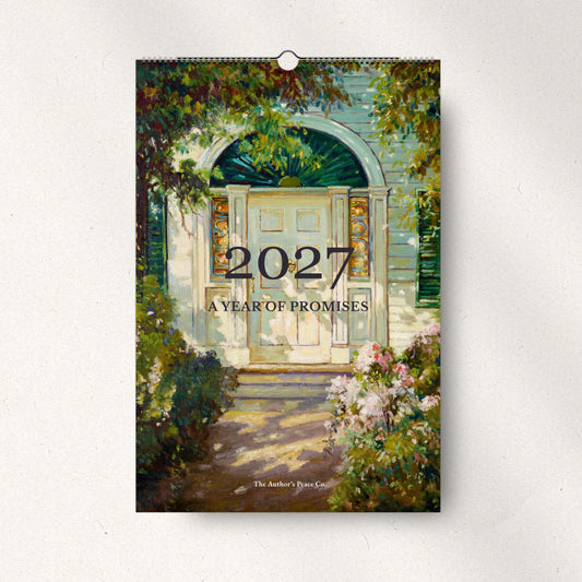 A spiral-bound 2027 wall calendar titled 'A Year of Promises' hangs on a light gray wall. The cover features a painted scene of a white arched door with green foliage and pink flowers.