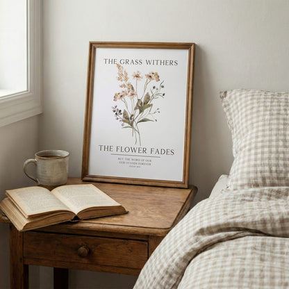 Framed artwork with floral design and text on a wooden nightstand next to an open book and mug.