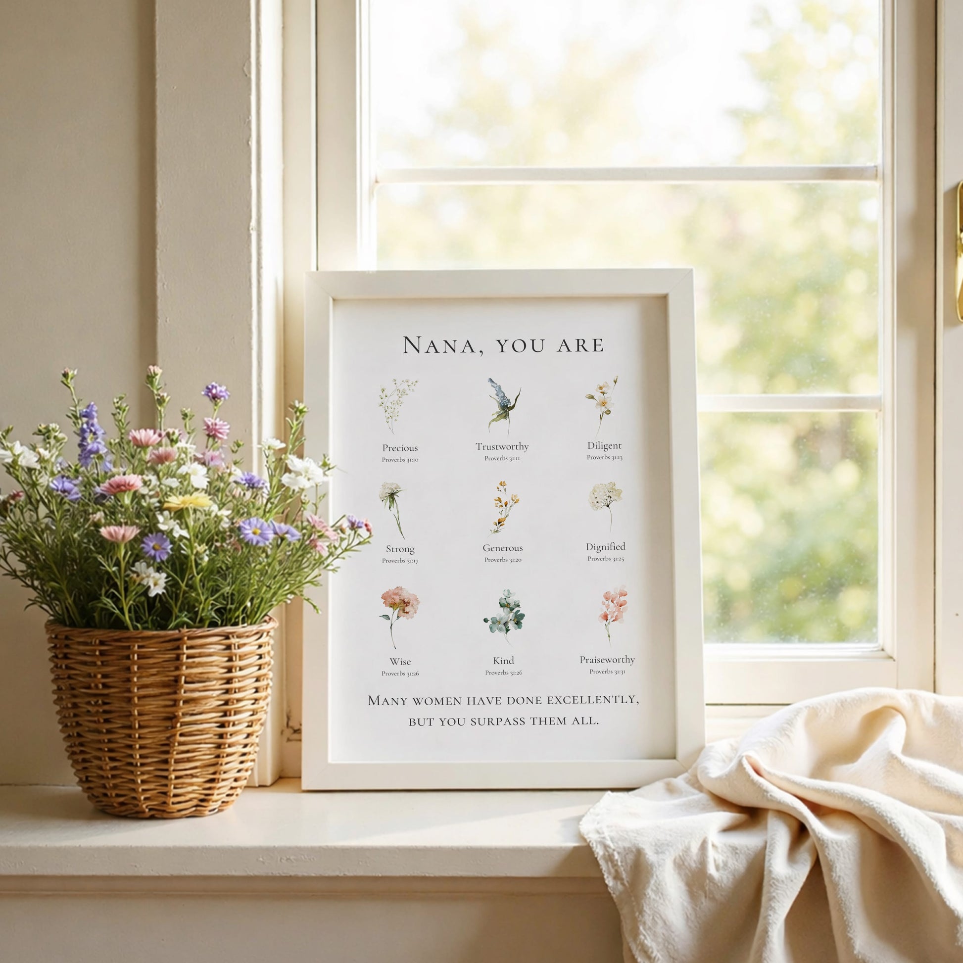 Framed print with floral illustrations and text on a windowsill with flowers and a blanket.