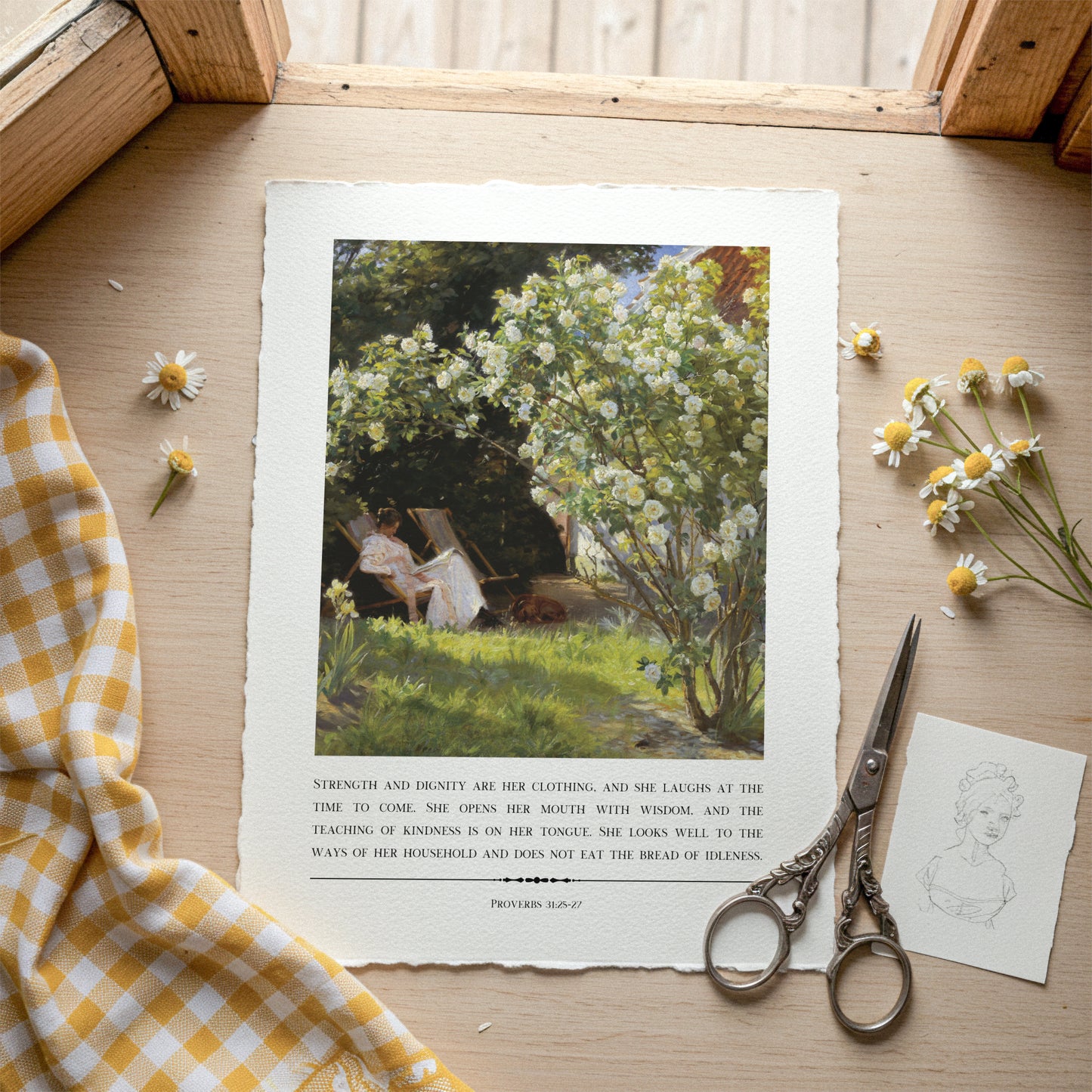 Printed artwork of a woman in a garden with flowers, placed on a wooden surface with a checkered cloth and scissors.