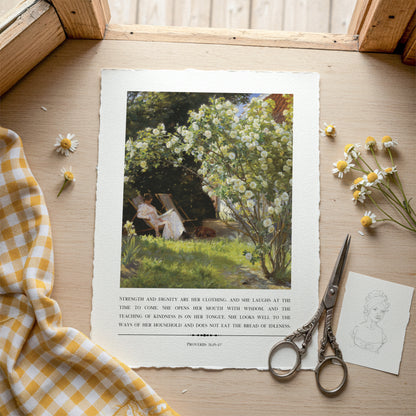 Printed artwork of a woman in a garden with flowers, placed on a wooden surface with a checkered cloth and scissors.