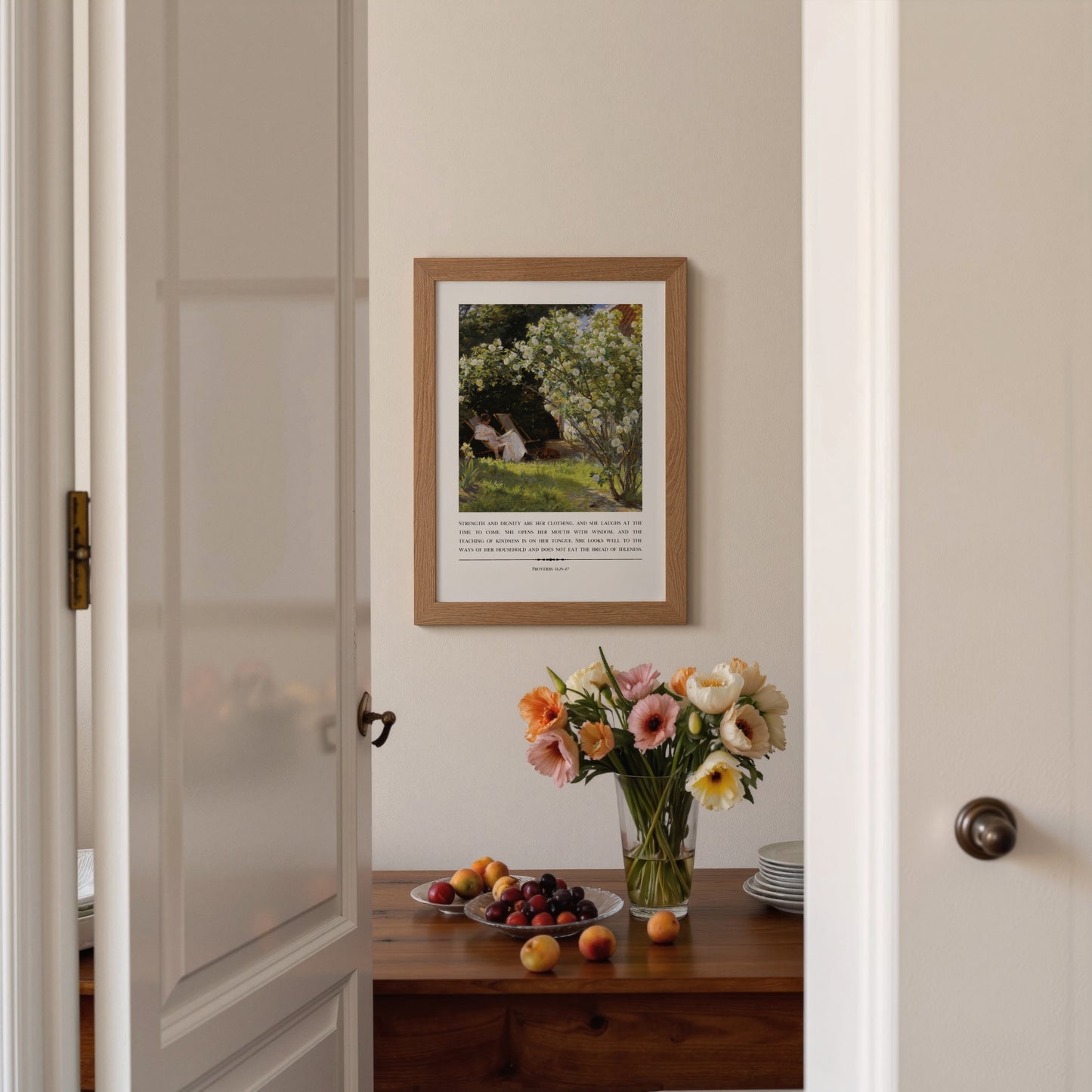 Framed artwork on a wall with a table displaying flowers and fruit.