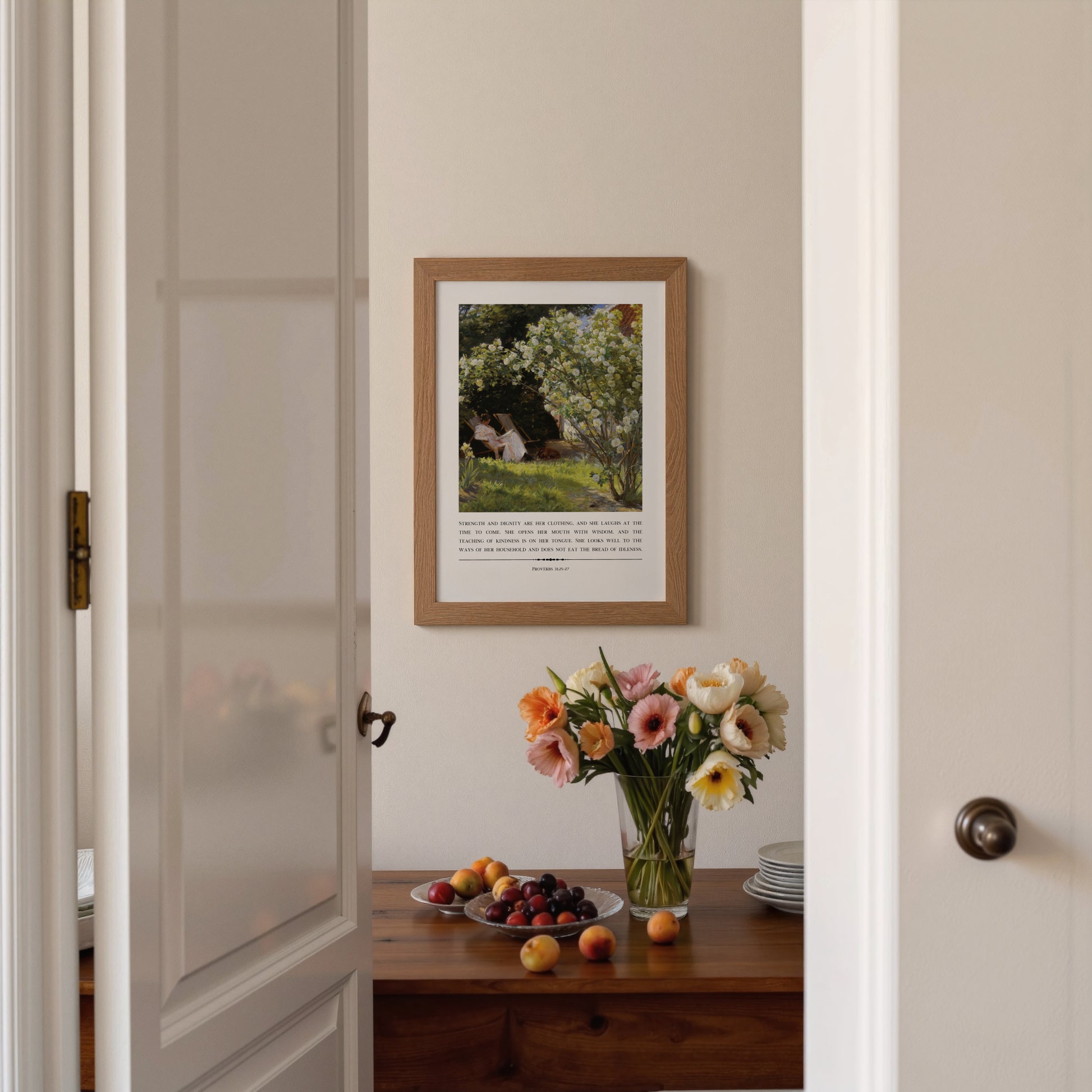 Framed artwork on a wall with a table displaying flowers and fruit.