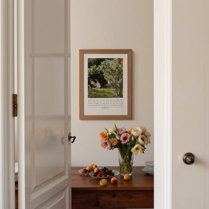 Framed artwork on a wall with a table displaying flowers and fruit.