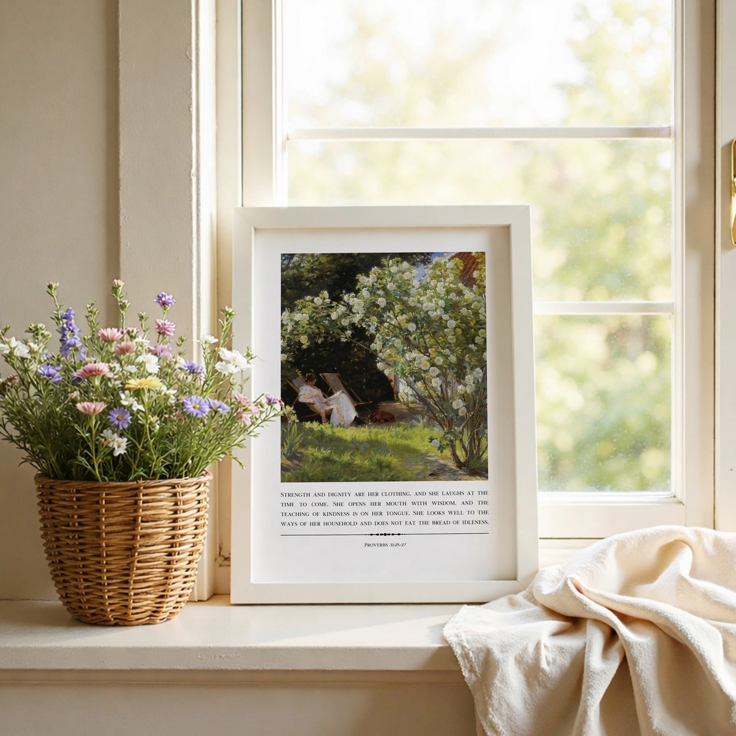 Framed artwork on a windowsill with flowers and a blanket