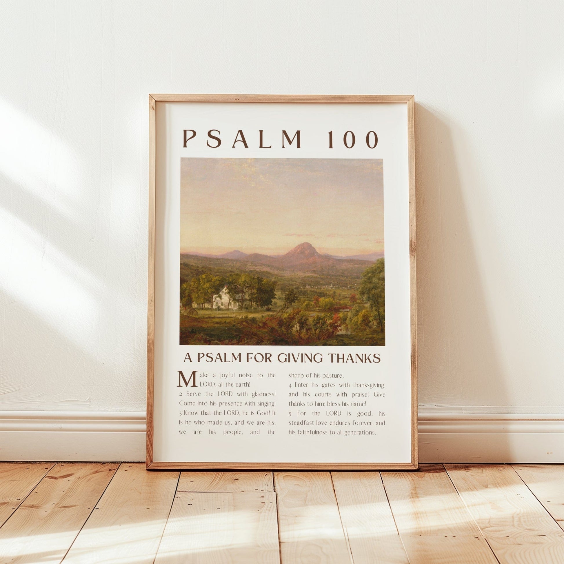 Framed poster with 'Psalm 100' text and landscape illustration on a wooden floor.