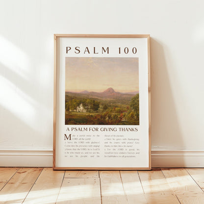 Framed poster with 'Psalm 100' text and landscape illustration on a wooden floor.