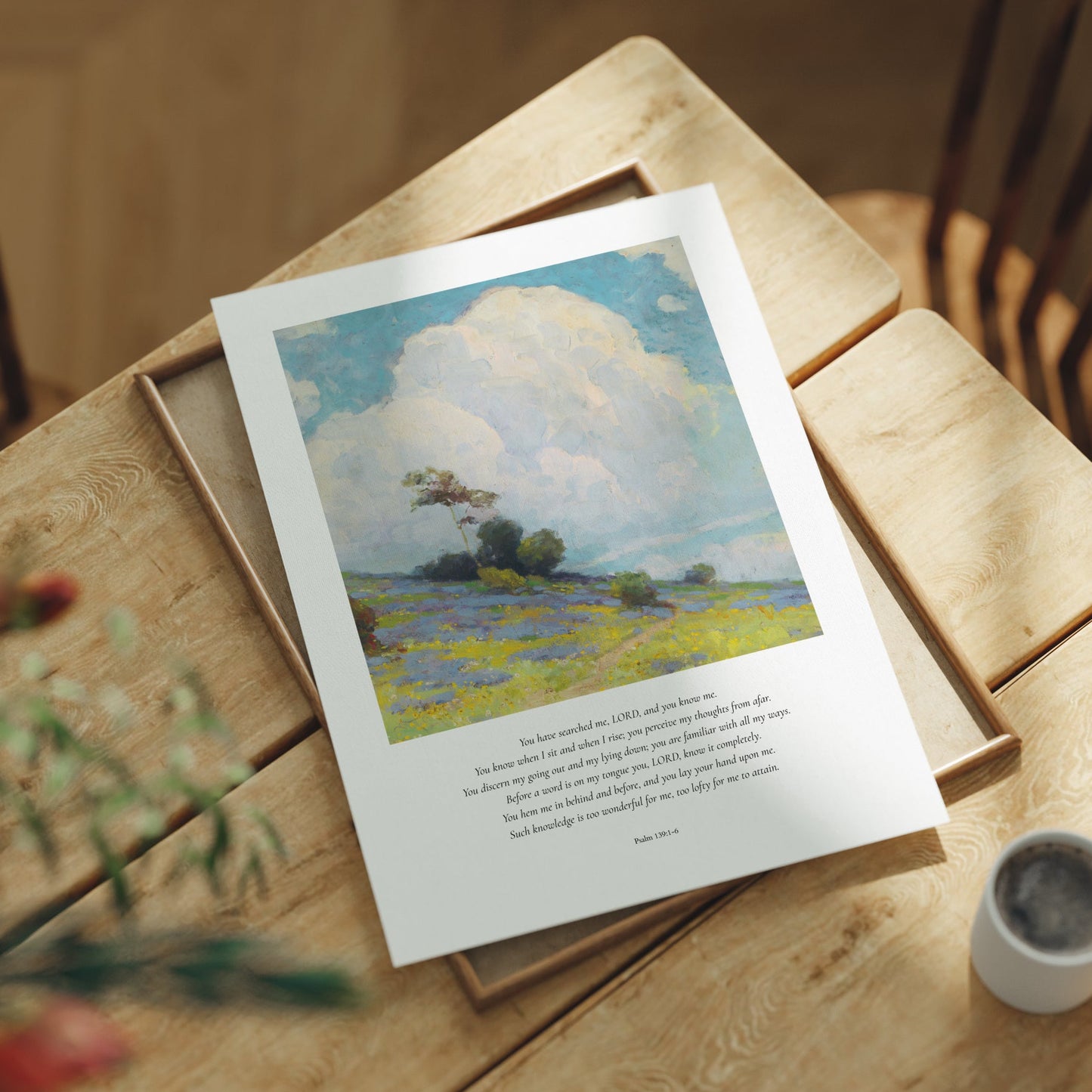 Framed artwork on a wooden table with a cup and plant in the background