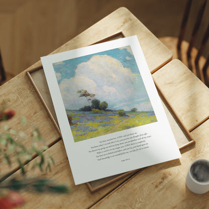 Framed artwork on a wooden table with a cup and plant in the background