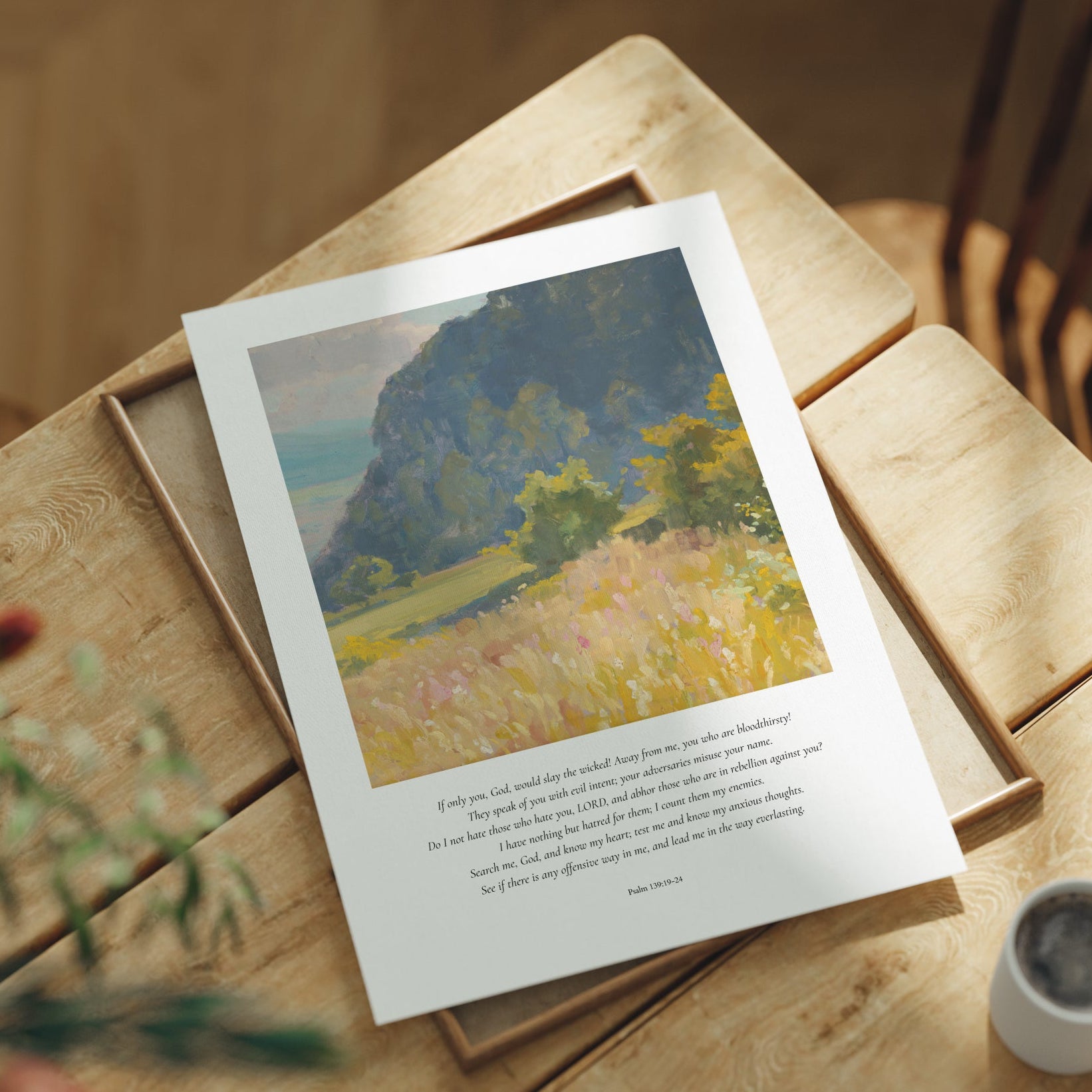 Framed artwork on a wooden table with a cup and plant in the background