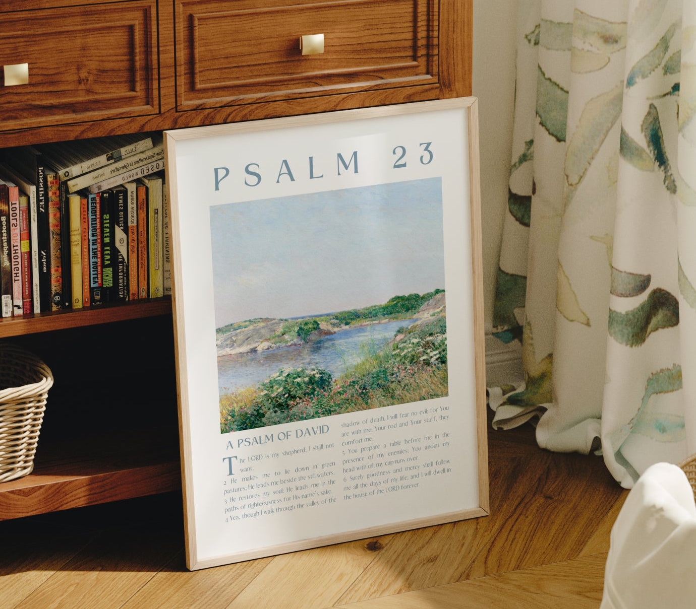 Wooden sideboard with books, a framed poster of Psalm 23, and a chair in a room with a window and curtains.