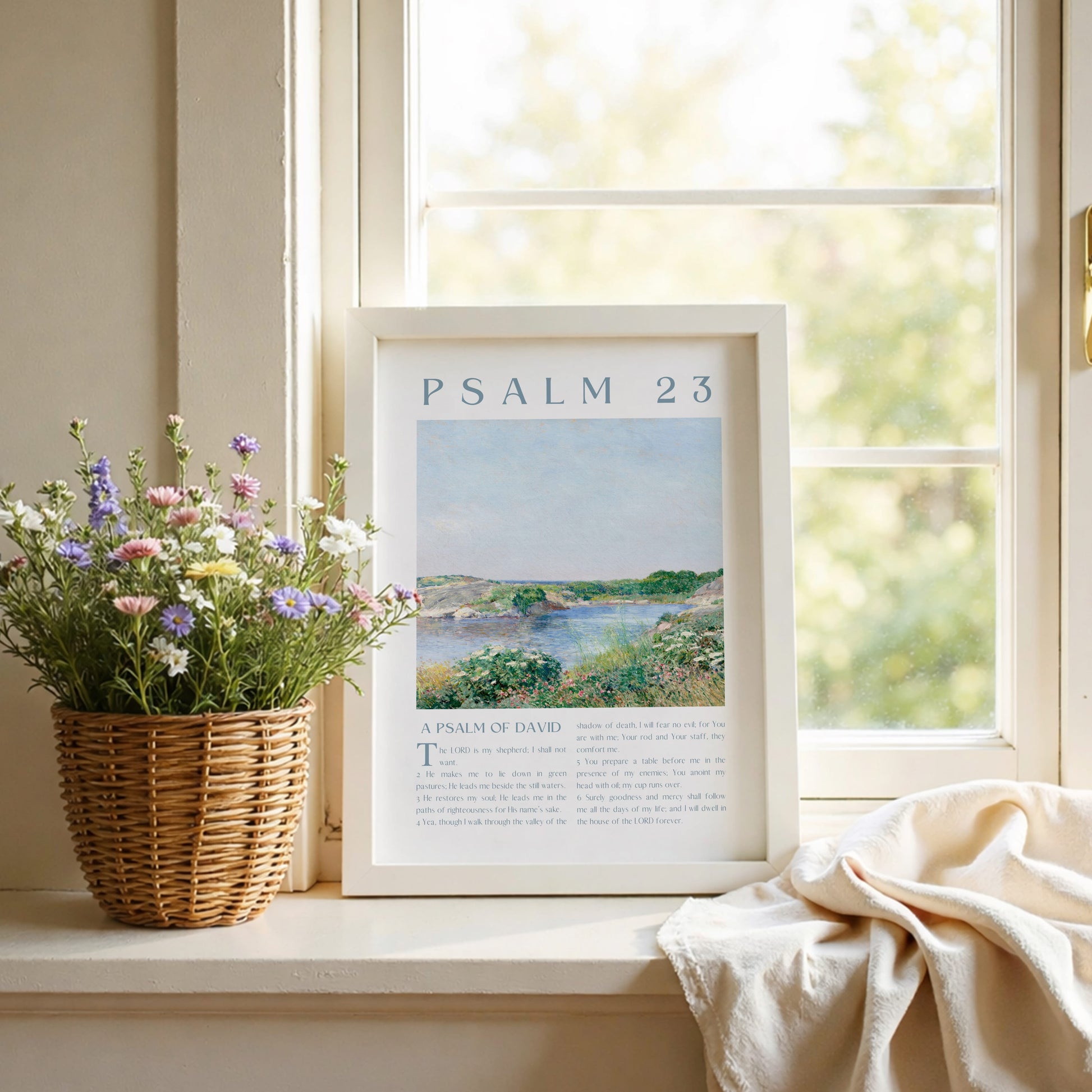 Framed 'Psalm 23' print on a windowsill with flowers and a blanket.