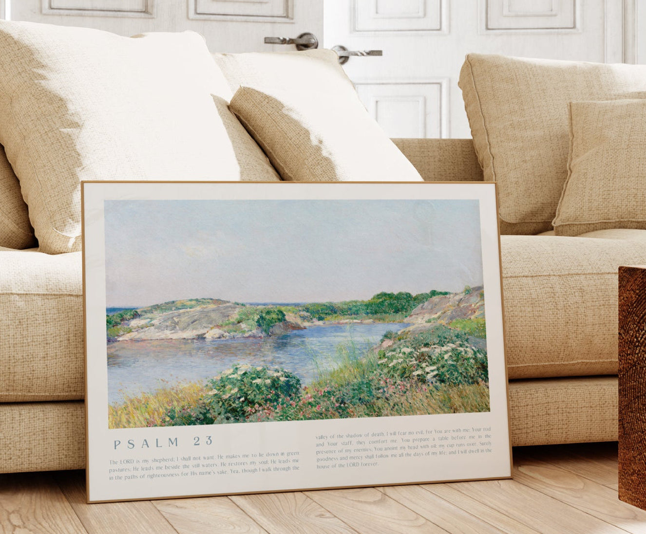 Framed landscape print on a wooden floor in a living room with a beige sofa.