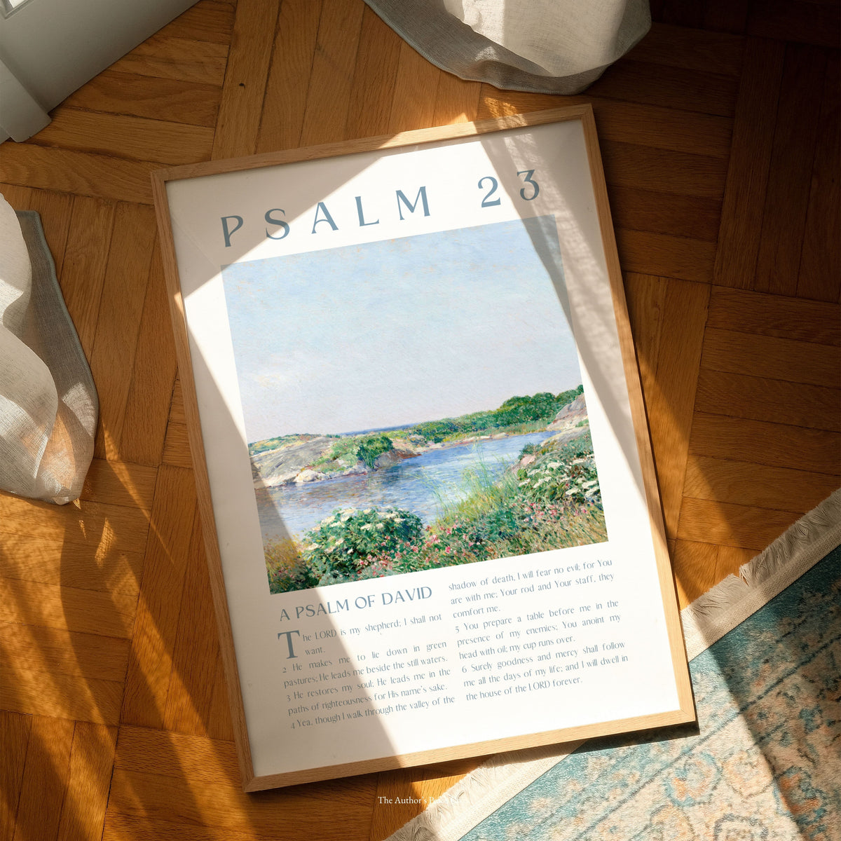 A framed art print of Psalm 23 displayed on a wooden parquet floor, angled slightly with natural sunlight casting shadows across it.