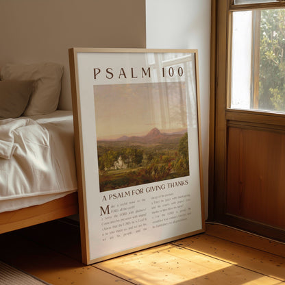 Framed poster titled 'Psalm 100' on a wooden floor next to a bed.