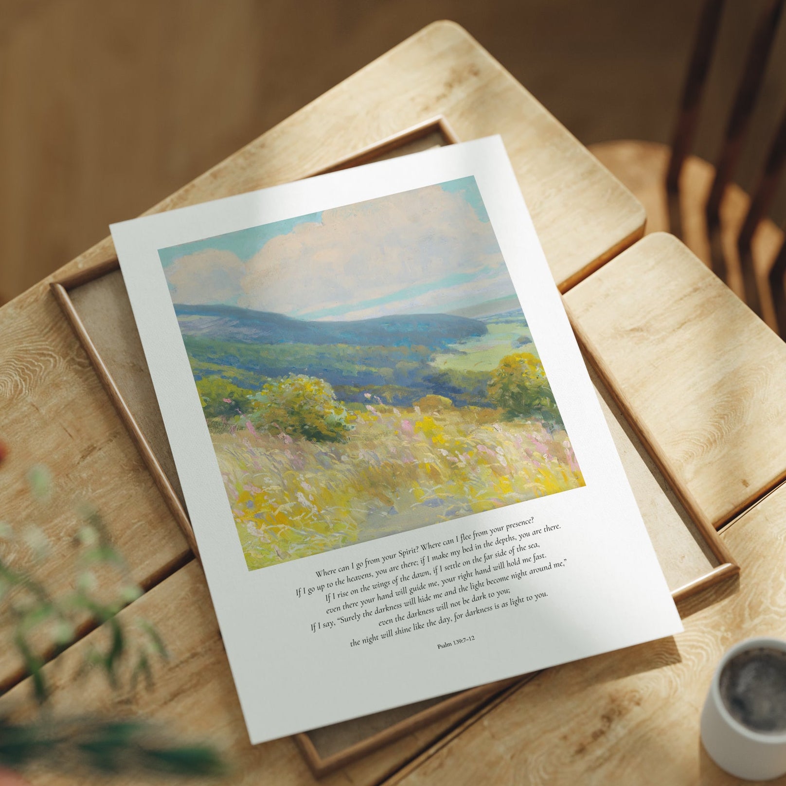 Framed landscape print on a wooden table with a cup and plant in the background