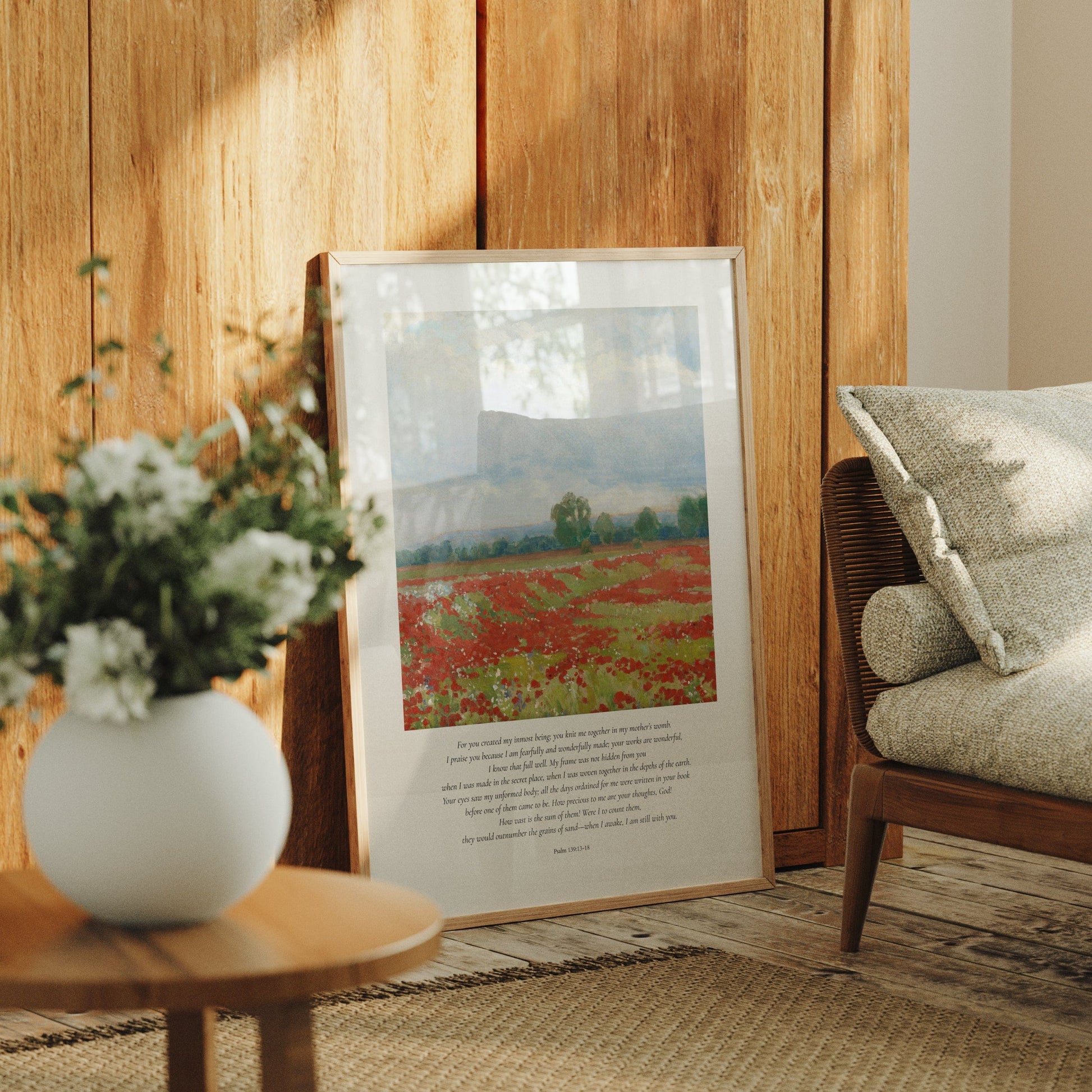 Framed artwork of a landscape with flowers and a chair in a room with wooden walls.