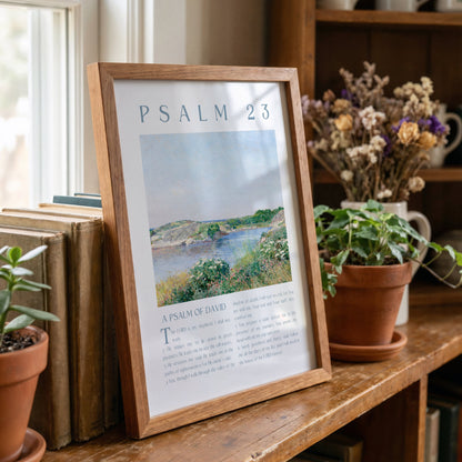 Framed poster of Psalm 23 on a wooden shelf with books and plants.