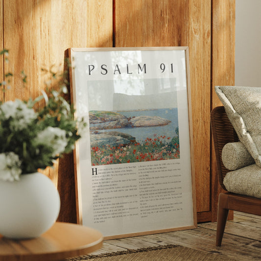 A framed art print of Psalm 91 leaning against a wooden wall in a cozy room setting, next to a white flower vase and a woven armchair.